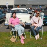 Zwei Frauen auf Campingstühlen vor Oldtimern