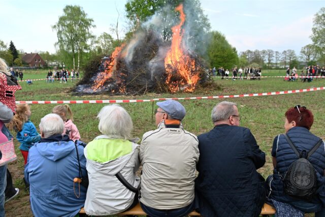 Ein Osterfeuer brennt, Menschen sitzen und stehen drumherum und gucken es sich an.