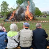 Ein Osterfeuer brennt, Menschen sitzen und stehen drumherum und gucken es sich an.