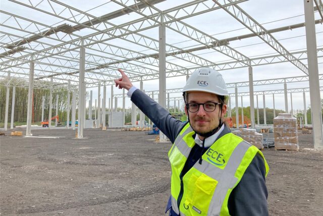 Ein Mann mit Helm und Warnweste unter einer Stahlkonstruktion.