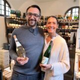 Sebastian Banhold und Daniela Münster stehen im Ladenlokal feinherb & konsorten und halten jeweils eine Flasche Wein in der Hand.
