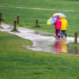Zwei Kinder laufen in einem Park durch eine große Pfütze.