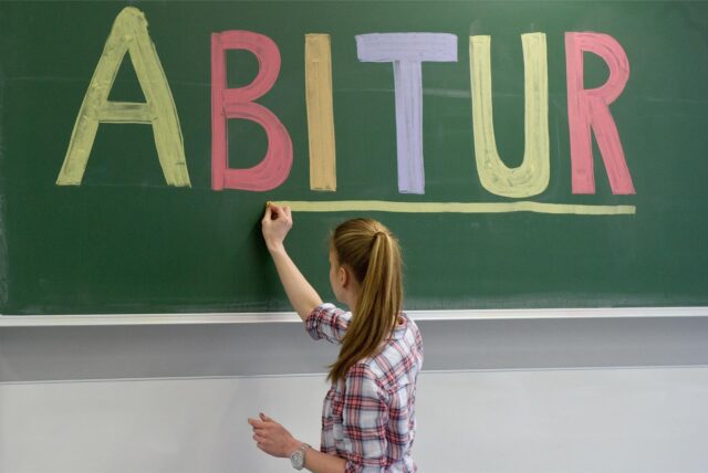 Eine Schülerin schreibt in einer Schule in NRW in großen und bunten Buchstaben das Wort „Abitur“ an die Tafel.