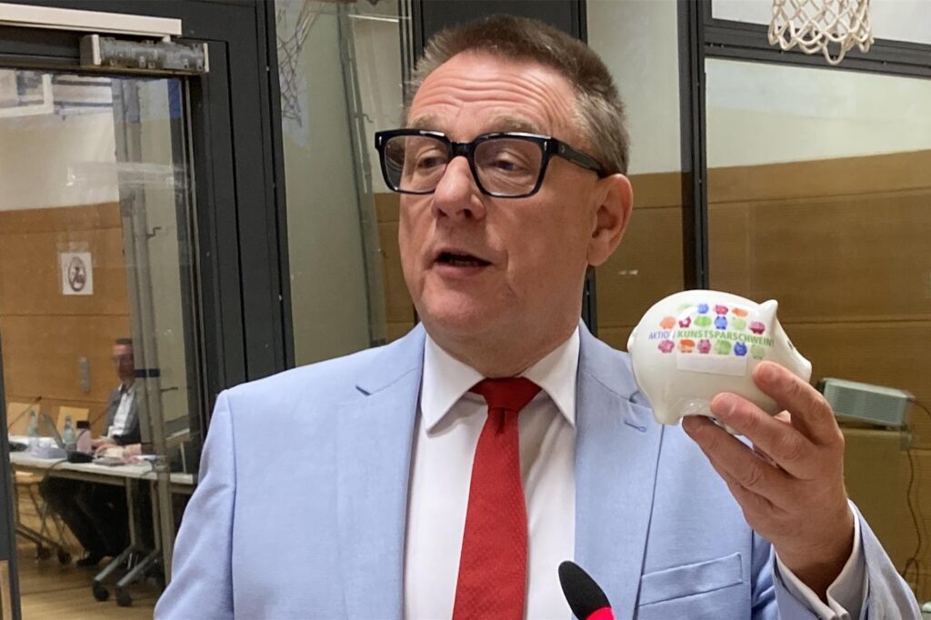 SPD-Fraktionschef Peter Wenzel hält symbolisch ein Sparschwein in der Hand.