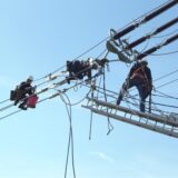 Drei Mitarbeiter von Amprion hängen Leiterseile und Isolatorenketten auf. Die Isolatoren sorgen dafür, dass die Leiterseile sicher befestigt sind und kein Strom auf Masten oder andere Bauteile übertritt.