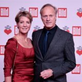 Gerhard Delling und Christina Block stehen vor einer Werbewand bei der Spendengala „Ein Herz für Kinder“ auf dem Roten Teppich an.