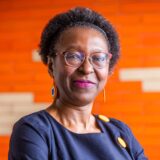 Porträtfoto von Vaye Tatah vor einer orangefarbenen Wand in ihrem Büro in Dortmund, in dem auch der Redaktionssitz des Magazins Africa Positive untergebracht ist.