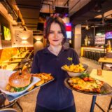 Eine Mitarbeiterin des Dortmunder Bistro 09 hält Teller mit Burger, Pommes und Schnitzel lächelnd in die Kamera