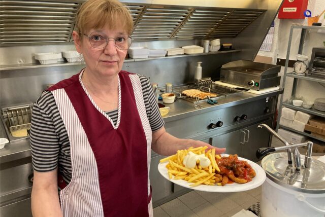 Eine Mitarbeiterin serviert einen Teller mit Pommes und Krüstchen.