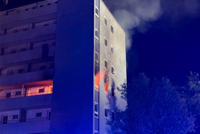 Flammen schlagen aus einer Wohnung eines Mehrfamilienhauses.