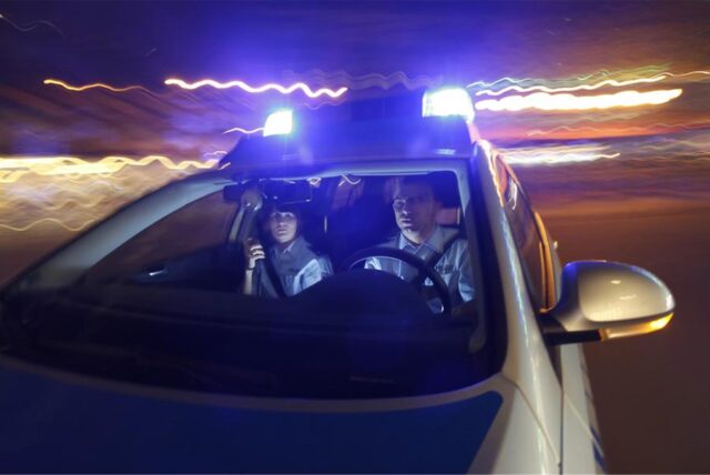 Ein Polizeiwagen fährt nachts durch eine Straße.