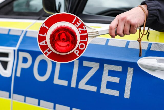 Ein Polizist hält eine Polizeikelle für eine Kontrolle auf einem Parkplatz an der Autobahn