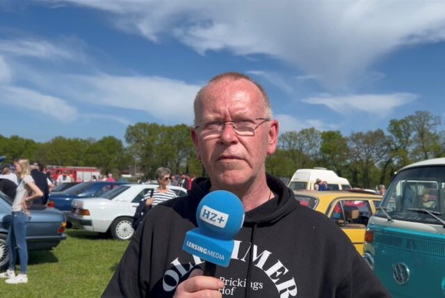Veranstalter mit Mikrofon in der Hand vor Autos stehend und spricht.