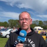 Veranstalter mit Mikrofon in der Hand vor Autos stehend und spricht.