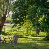 Eine Tisch und Gartenstühle auf einer Wiese im Freien im Schatten von Bäumen.