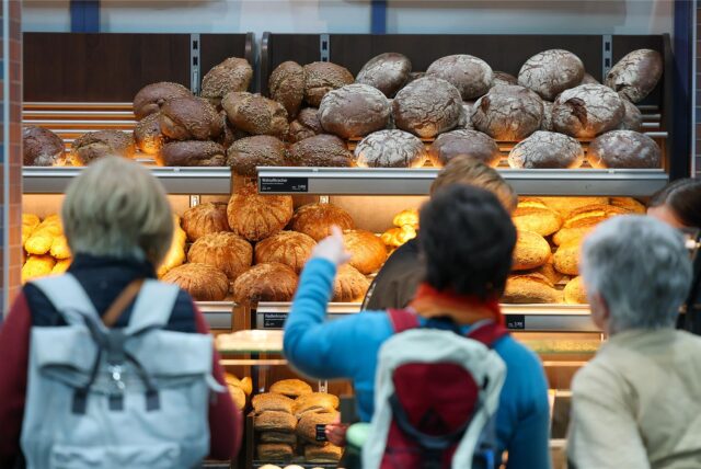 Kunden stehen vor einer Auslage in einer Bäckerei.