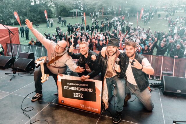 Band mit Schild „Gewinnerband 2022“ auf der Bühne, dahinter Publikum.