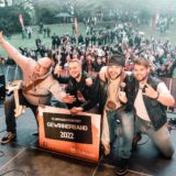 Band mit Schild „Gewinnerband 2022“ auf der Bühne, dahinter Publikum.