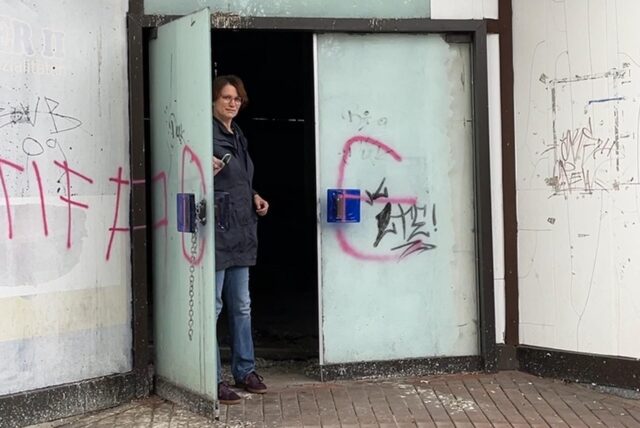 Eine Frau steht neben der offenen Tür eines leerstehenden Gebäudes.
