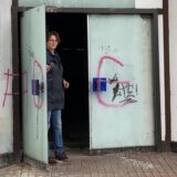 Eine Frau steht neben der offenen Tür eines leerstehenden Gebäudes.