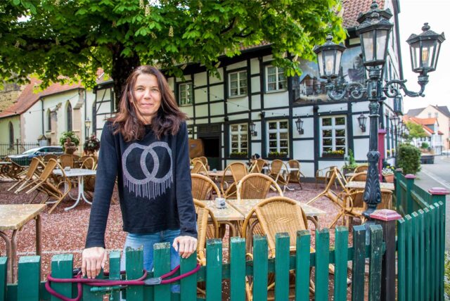 Geschäftsführerin Tatjana Schüle lehnt sich am Restaurant Alt Westerholt in Herten-Westerholt auf einen grünen Holzzaun, der den Biergarten der Gastronomie umgibt.