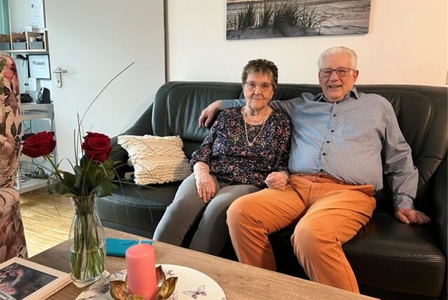 Rolf und Marlies Heusinger sitzen auf der Couch in ihrer Wohnung, Rolf hält Marlies im Arm.