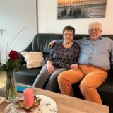 Rolf und Marlies Heusinger sitzen auf der Couch in ihrer Wohnung, Rolf hält Marlies im Arm.