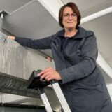 Eine Frau steht auf einer Leiter und lächelt in die Kamera.