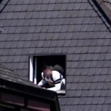 Ein junger Mann schaut aus dem Fenster eines Wohnhauses heraus. Sein Gesicht ist unkenntlich gemacht worden.
