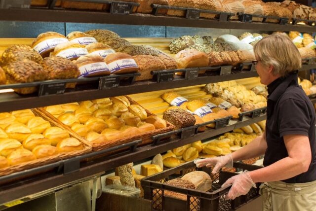 Eine Bäckerei-Fachverkäuferin sortiert Brote aus dem Korb ins Regal.
