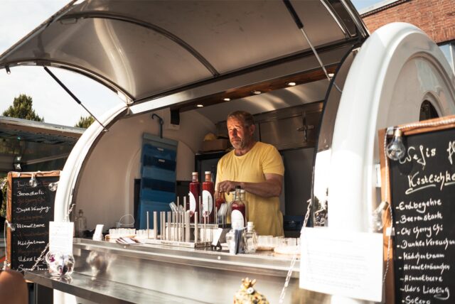 Ein Mann steht in seinem Foodtruck und hält Soßen in seiner Hand.