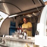 Ein Mann steht in seinem Foodtruck und hält Soßen in seiner Hand.