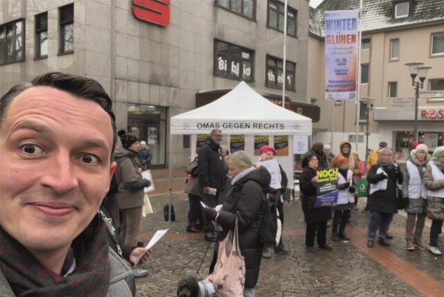 Mehrere Omas mit Sonnenbrille halten auf einer Straße ein Transparent mit der Aufschrift „Beharrlich für Menschenwürde und Demokratie“ hoch.