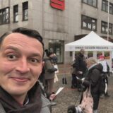 Mehrere Omas mit Sonnenbrille halten auf einer Straße ein Transparent mit der Aufschrift „Beharrlich für Menschenwürde und Demokratie“ hoch.