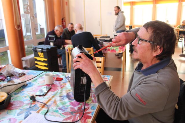 Ein Mann sitzt beim Repai-Café im Februar 2025 im Gemeindezentrum der Thomaskirche in Westerholt an einem Tisch, hält ein Elektrogerät in der linken und einen Schraubendreher in der rechten Hand.