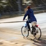 Eine Fahrradfahrerin fährt am Abend bei Schneefall über eine Straße