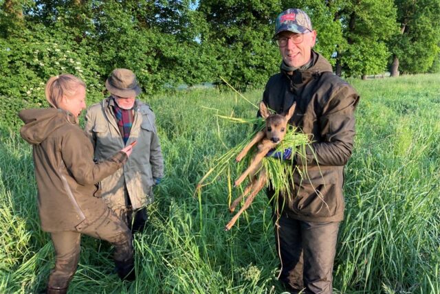 Menschen stehen auf einem Feld, einer hält ein Kitz in den Händen.