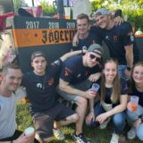 Eine Gruppe junger Menschen sitzt, steht vor dem Jägermeisterwagen und grinsen in die Kamera.