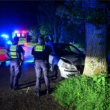 Polizisten stehen vor einem Auto, das gegen einen Baum geprallt ist.