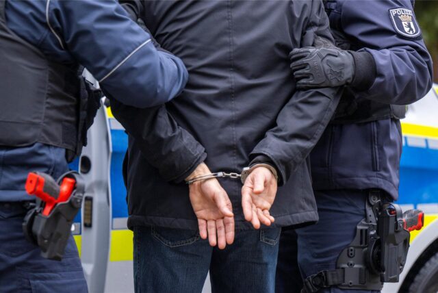 in Mann wird von zwei Polizisten festgenommen. Die Beamten führen den Mann mit Handschellen ab.
