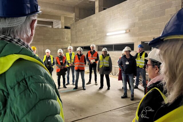 Menschen mit Helmen und in Warnwesten besichtigen eine Baustelle