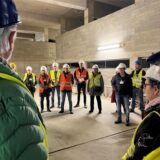 Menschen mit Helmen und in Warnwesten besichtigen eine Baustelle