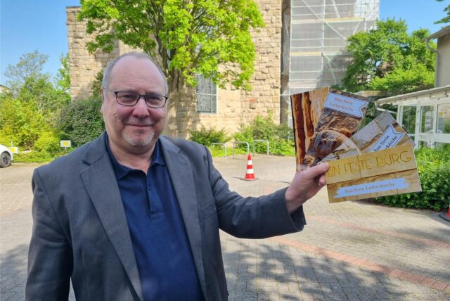 Ein Mann steht vor der Lutherkirche in Datteln und hält vier Karten in der Hand.