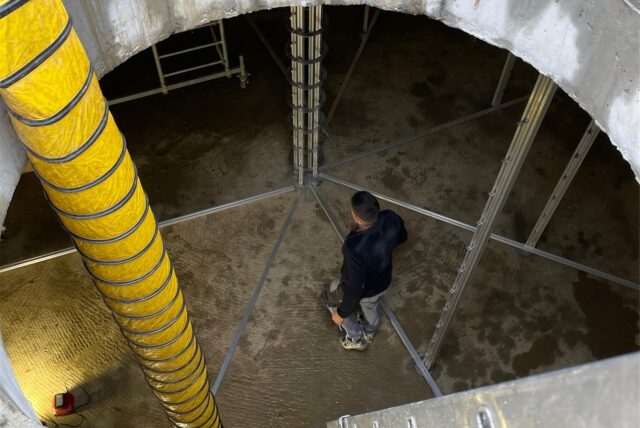 Ein Schlauch führt hinunter in den Eisspeicher des Solarhauses in Kamen. Unten steht ein Mann.