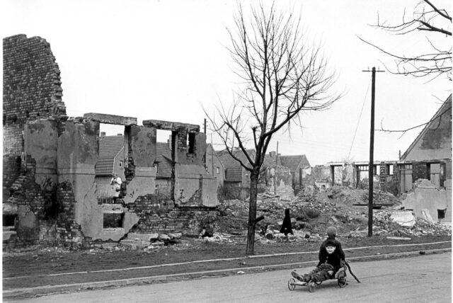 Ein Kind sitzt 1945 auf einem Wagen vor den Ruinen zerstörter Häuser in der Zechenstraße in Datteln.