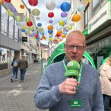 RZ-Redakteur Markus Geling steht mit grünem Mikrofon auf der Großen Geldstraße in Recklinghausen. Bunte Lampions sind über die Straße gespannt.