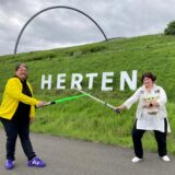 Heidi Fischer (r.) und ihre Nichte Sonja Kipper halten Laser-Schwerter und eine Stars-Wars-Figur in den Händen und posieren vor dem Herten-Schriftzug auf der Halde Hoheward in Herten.