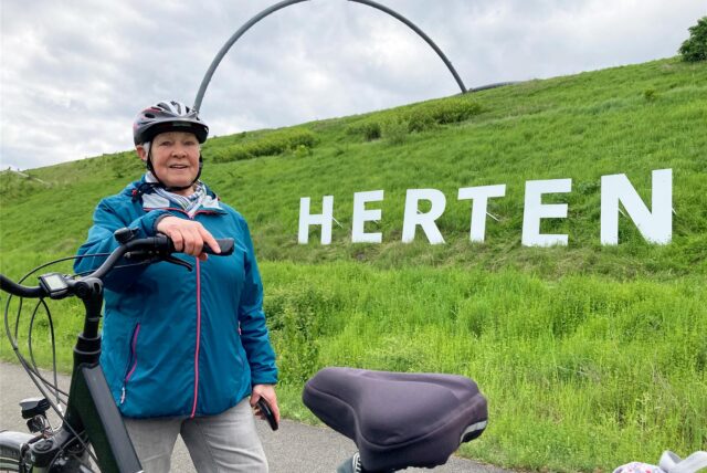 Die Hertenerin Petra Laugell steht an ihrem Fahrrad vor dem Herten-Schriftzug auf der Halde Hoheward.