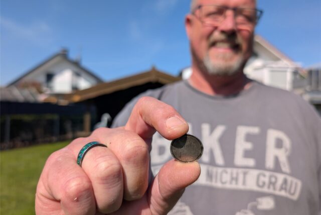 Gunther Berse hält seinen wiedergefundenen Kettenanhänger zwischen Daumen und Zeigefinger.