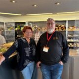 Edeltraud Hartelt und Wolfgang Schulz stehen im Vordergrund. Hinter ihnen sind die gefüllten Regale der Tafel zu sehen.